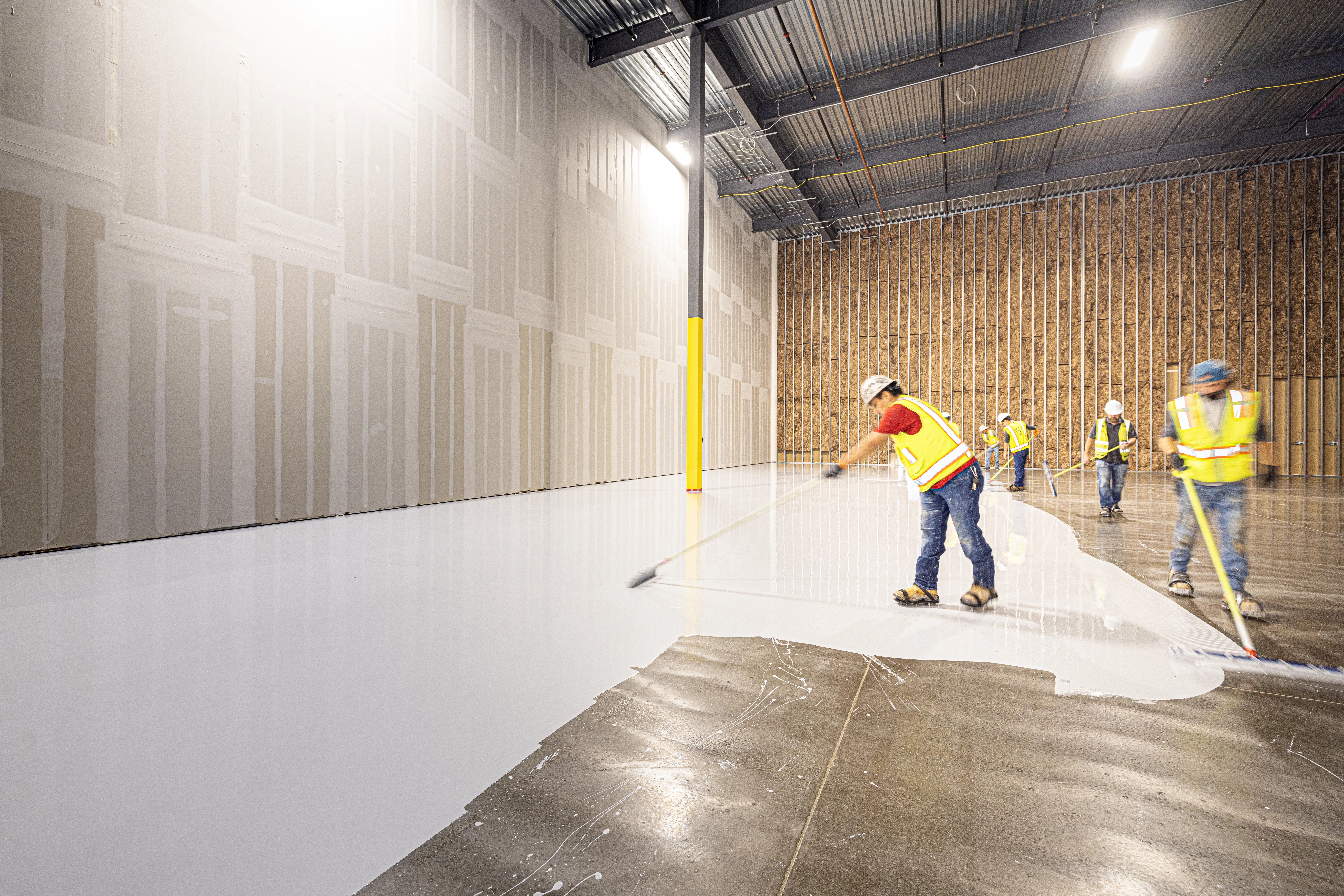 Crew applying epoxy floor coating across a large commercial space by Beyond Briks