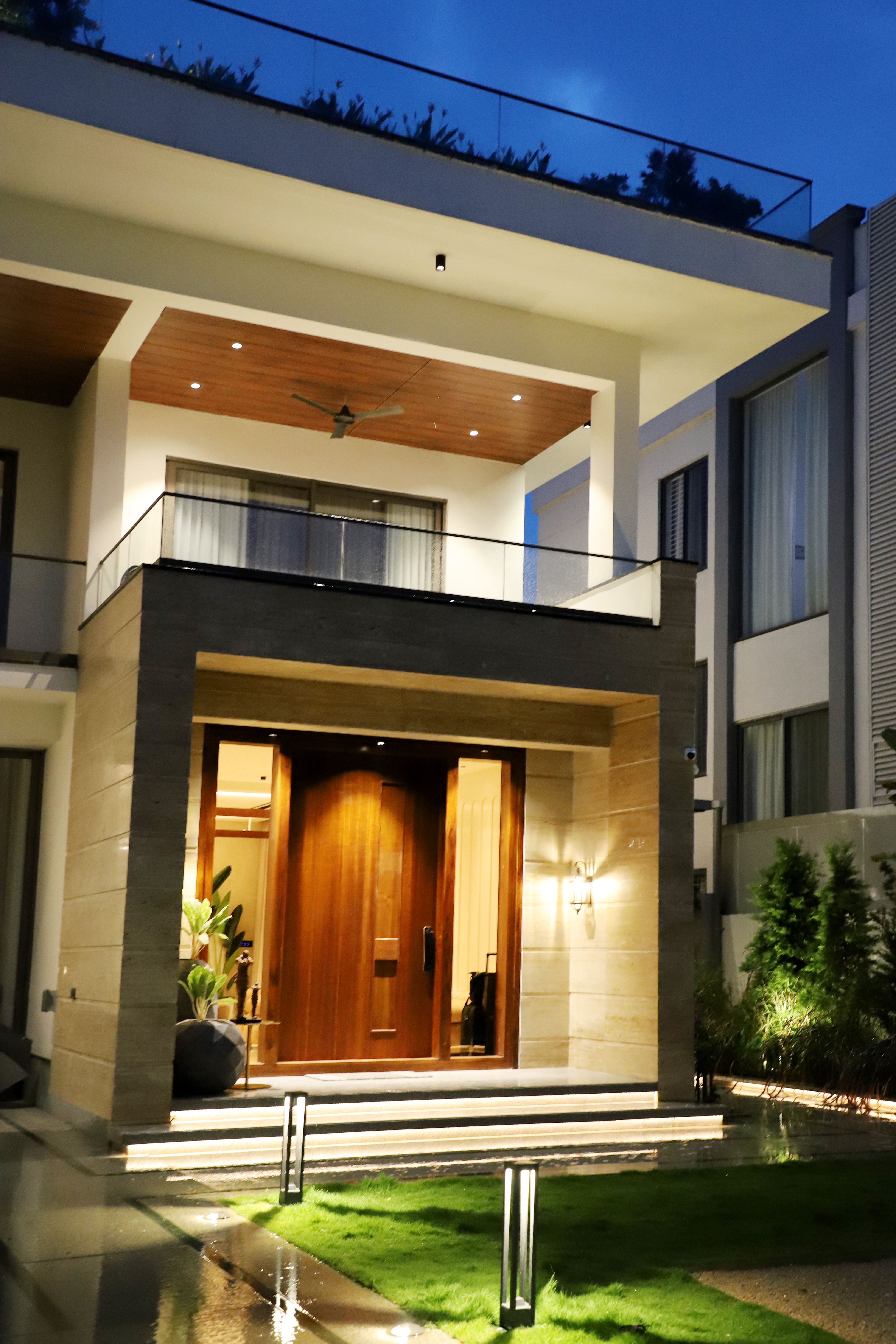 Luxury bungalow exterior with illuminated wooden entrance by Beyond Briks
